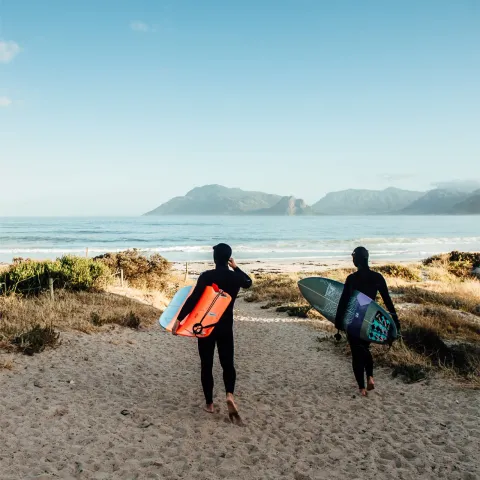Due ragazzi con la tavola da surf camminano sulla spiaggia, con le montagne alle spalle