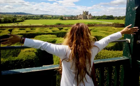 Una ragazza allarga le braccia davanti al labirinto di siepi e al castello