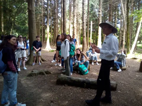Lezione all'aperto nel bosco: l'insegnante parla al gruppo seduto fra gli alberi