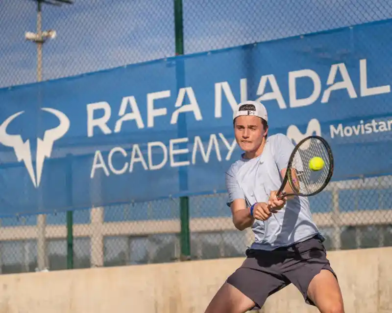 Un ragazzo colpisce di rovescio davanti allo striscione della Rafa Nadal Academy