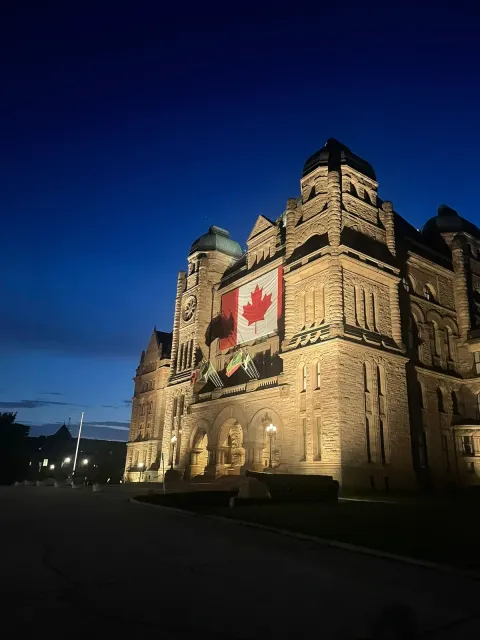 Un edificio storico illuminato di sera, con la bandiera canadese sulla facciata